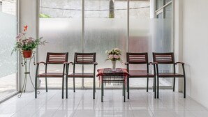 A seating area with four wooden chairs and a table, a potted plant, and a window with a view of the outside. - RedDoorz Plus @ Gunungsari Surabaya (Surabaya)
