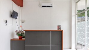 A reception desk with a grey partition, a mounted air conditioner, a television, and a potted plant. - RedDoorz Plus @ Gunungsari Surabaya (Surabaya)