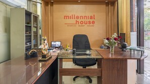 A reception desk with a wooden backdrop and the text "millennial house SYARIAH GUEST HOUSE". - RedDoorz Syariah @ Danau Kerinci Sawojajar (Malang)