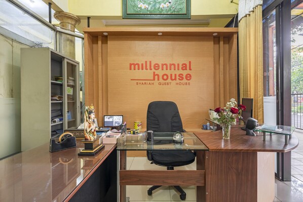 A reception desk with a wooden backdrop and the text "millennial house SYARIAH GUEST HOUSE".
