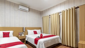 A hotel room with two beds, a wooden headboard, a nightstand with a lamp, and a window with beige curtains. - RedDoorz Syariah @ Danau Kerinci Sawojajar (Malang)