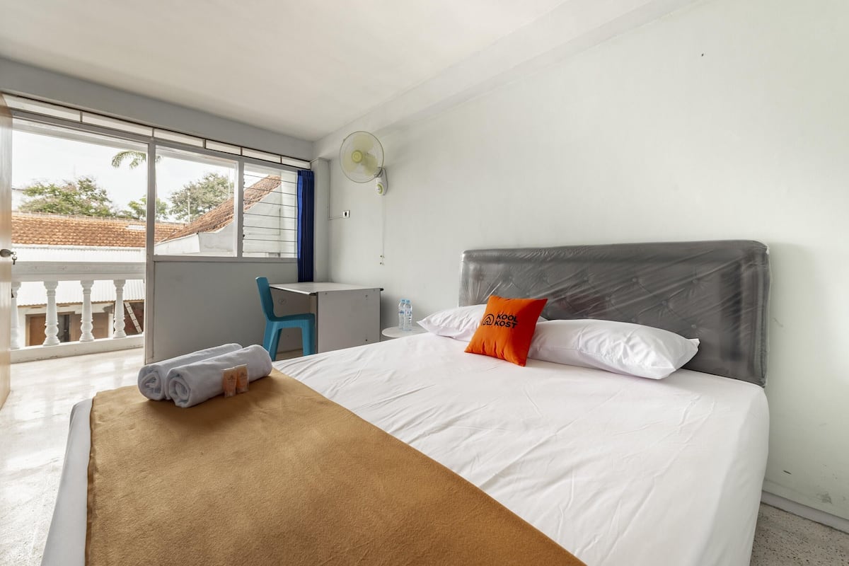 A hotel room with a bed, a desk, a chair, a window with a view, and a ceiling fan.