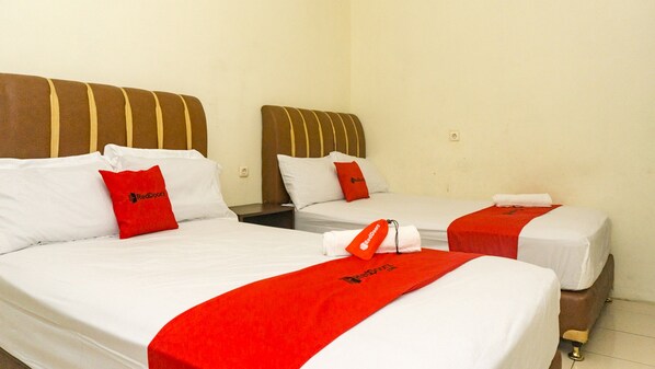 Two single beds with white linens and red accents, including pillows and a blanket. Each bed has a wooden headboard and a nightstand.