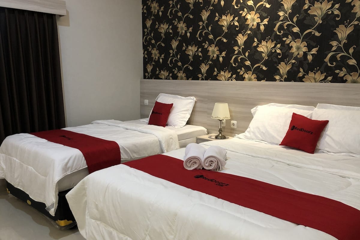 Hotellihuone, jossa on kaksi sänkyä, molemmissa valkoiset vuodevaatteet ja punaiset yksityiskohdat, yöpöytä lampun kanssa sekä kukkapainokuviollinen seinä.