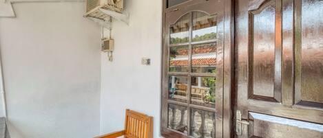 A room with a wooden bench, a window with a view of a traditional building, and an air conditioning unit mounted on the wall.