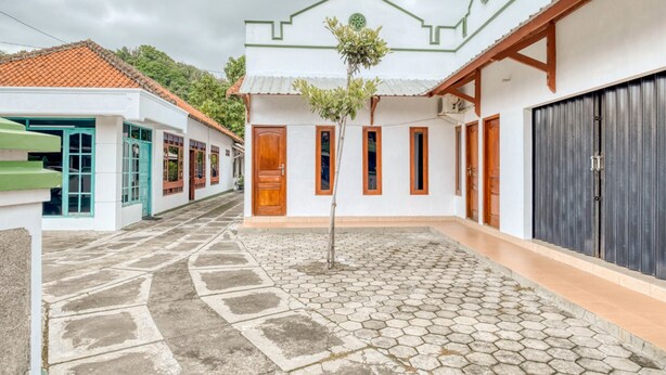 A courtyard with a tiled floor, a small tree, and buildings with doors and windows. - RedDoorz near Wisata Pantai Parangtritis (Parangtritis)