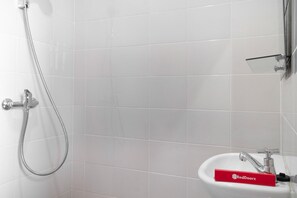 A bathroom with white tiles, a shower with a handheld hose, and a sink with a RedDoorz soap dispenser. - RedDoorz near Lippo Mall Puri (Jakarta)