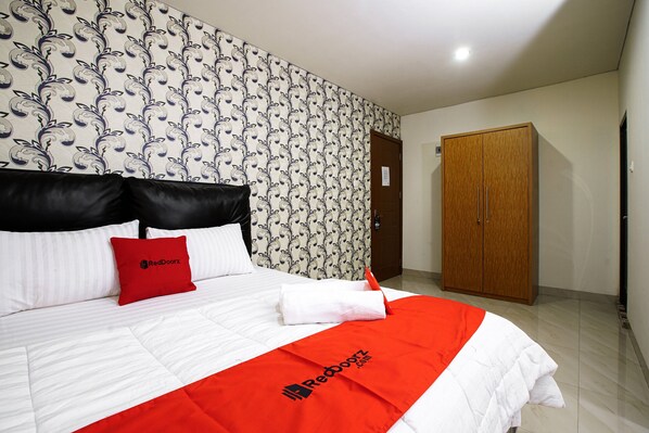 A hotel room with a bed, a red pillow, a white pillow, a red blanket, and a wooden wardrobe.