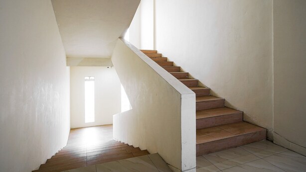 A staircase with wooden steps and white walls, leading to a room with a window. - RedDoorz near Palembang Trade Center 3 (Palembang)