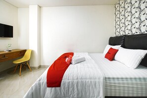 A hotel room with a bed, a desk, a chair, and a flat-screen TV on the wall.