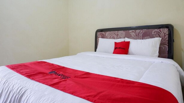 A bed with a white and red bedspread, a red pillow, and a headboard with a floral pattern. - RedDoorz near Lippo Plaza Buton (Bau-Bau)