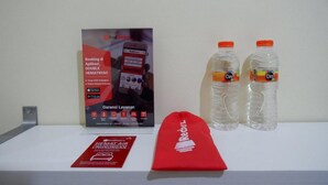 A promotional display with a RedDoorz sign, two water bottles, and a red RedDoorz bag on a white surface. - RedDoorz near Lippo Plaza Buton (Bau-Bau)