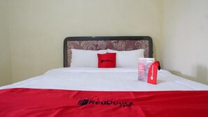 A neatly made bed with a red and white bedspread, a red pillow, and a RedDoorz.com brochure on the bed. - RedDoorz near Lippo Plaza Buton (Bau-Bau)