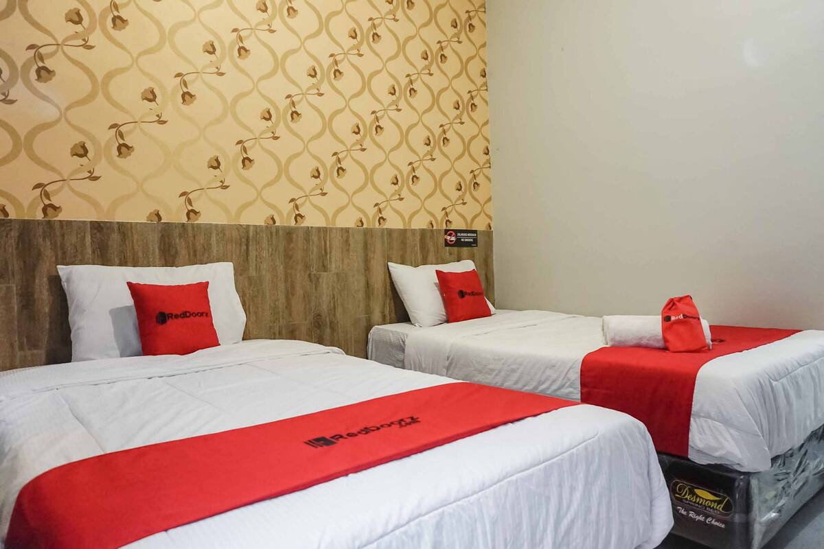 A hotel room with two beds, each with a red blanket and pillow, and a wooden headboard.