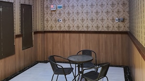 A room with patterned wallpaper, a wooden panel wall, a ceiling with blue LED lighting, and a small round table with four chairs. - RedDoorz near CitraLand Gama City Medan (Medan)
