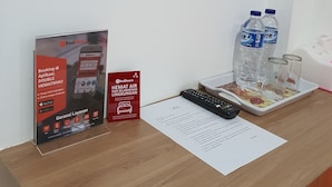 A reception desk with a RedDoorz sign, a remote control, a tray with water bottles and glasses, and a tissue box. - RedDoorz near CitraLand Gama City Medan (Medan)
