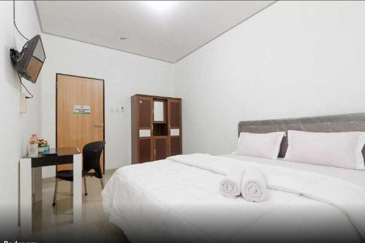 A hotel room with a bed, a desk, a chair, a wardrobe, and a television.