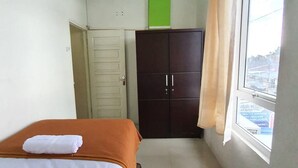 A bedroom with a bed, a wardrobe, a window, and a green cross on the wall. - KoolKost Syariah @ Medan Johor (Medan)
