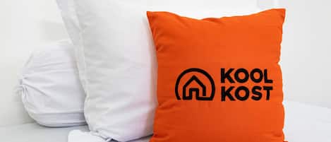 Two pillows, one white and one orange with a logo and text, on a white surface.