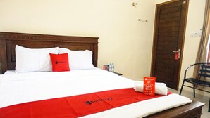 A neatly made bed with a red and white bedspread, a red pillow, and a towel with a RedDoorz logo.