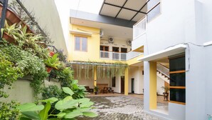 A courtyard with a brick floor, a yellow building with a balcony, and various plants.