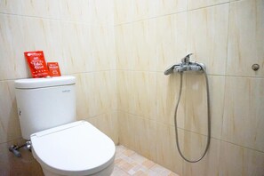 A bathroom with a toilet, a shower, and a toilet paper dispenser. - RedDoorz @ Jalan Kedawung (Malang)