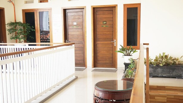 A hotel lobby with wooden doors numbered 202 and 201, a white railing, and potted plants.