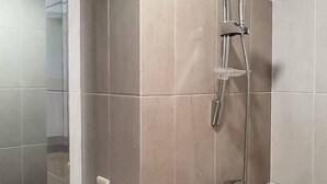 Un baño con ducha, paredes de azulejos y mampara de vidrio.