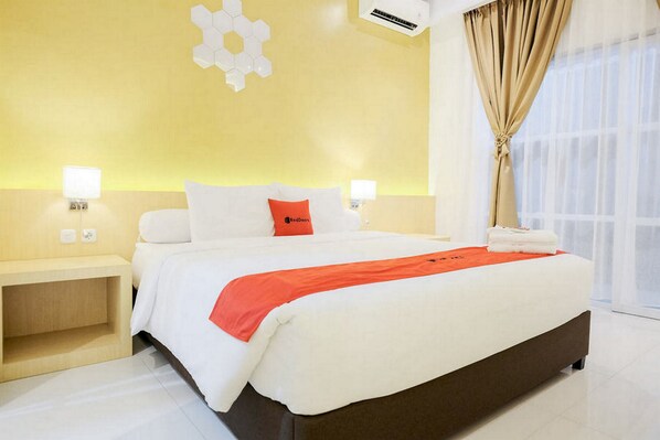 A hotel room with a large bed, two bedside tables, a wall-mounted air conditioner, and a window with curtains.