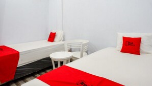 Habitació d'hotel amb dos llits individuals, cadascun amb manta i almoçada vermelles, una taula petita blanca i una cadira.
