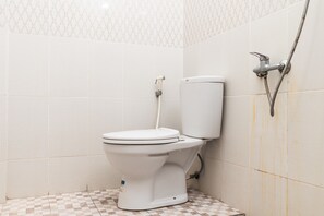 Des toilettes blanches avec une chasse d’eau, un flexible de douche et un sol carrelé.