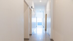 Un pasillo largo y estrecho con paredes blancas y piso de baldosas, que conduce a una habitación luminosa al final.