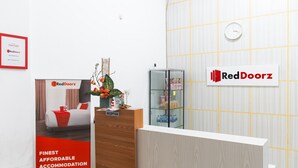 Un área de recepción con el letrero de RedDoorz, un mostrador de recepción, un reloj y un certificado enmarcado en la pared.