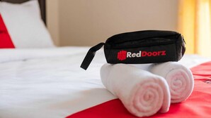A bed with white linens, a black bag with 'RedDoorz' branding, and two rolled towels. - RedDoorz @ Ruko ITC Roxy Mas (Jakarta)