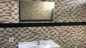 Une salle de bain avec un mur carrelé, un lavabo surmonté d’un miroir et une barre horizontale noire.