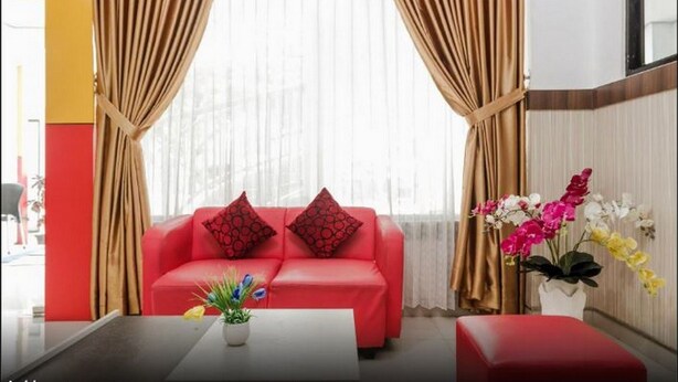 Un canapé rouge avec des coussins à motifs, une petite table sur laquelle est posée une plante, et un vase rempli de fleurs.