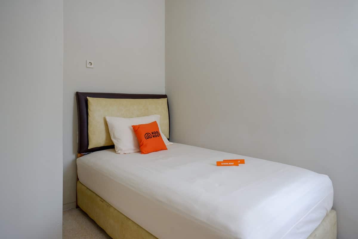 Una cama individual con colchón blanco, cabecera marrón y dos almohadas, una blanca y otra naranja con texto.