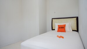 A single bed with white bedding and a headboard, a small orange pillow with a logo, and a white wall. - KoolKost Female Syariah near UII Taman Siswa (Yogyakarta)