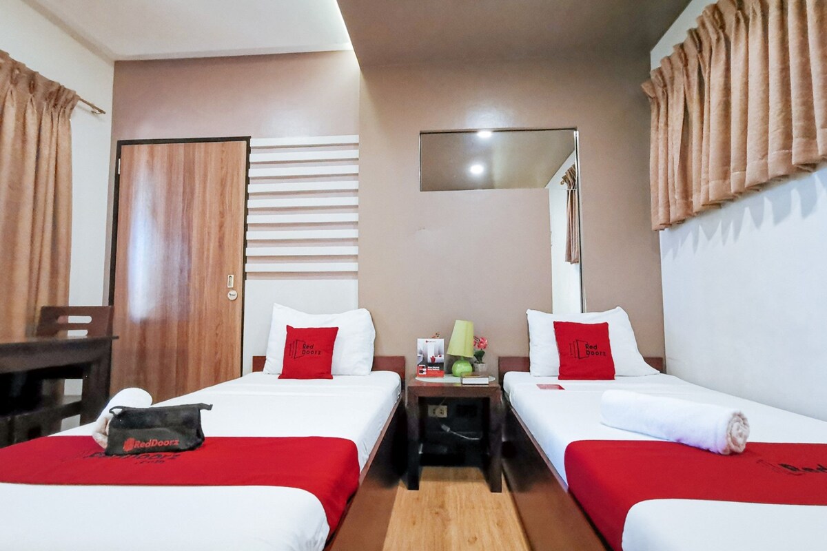 A hotel room with two beds, a desk, a chair, a nightstand, and a mirror on the wall.