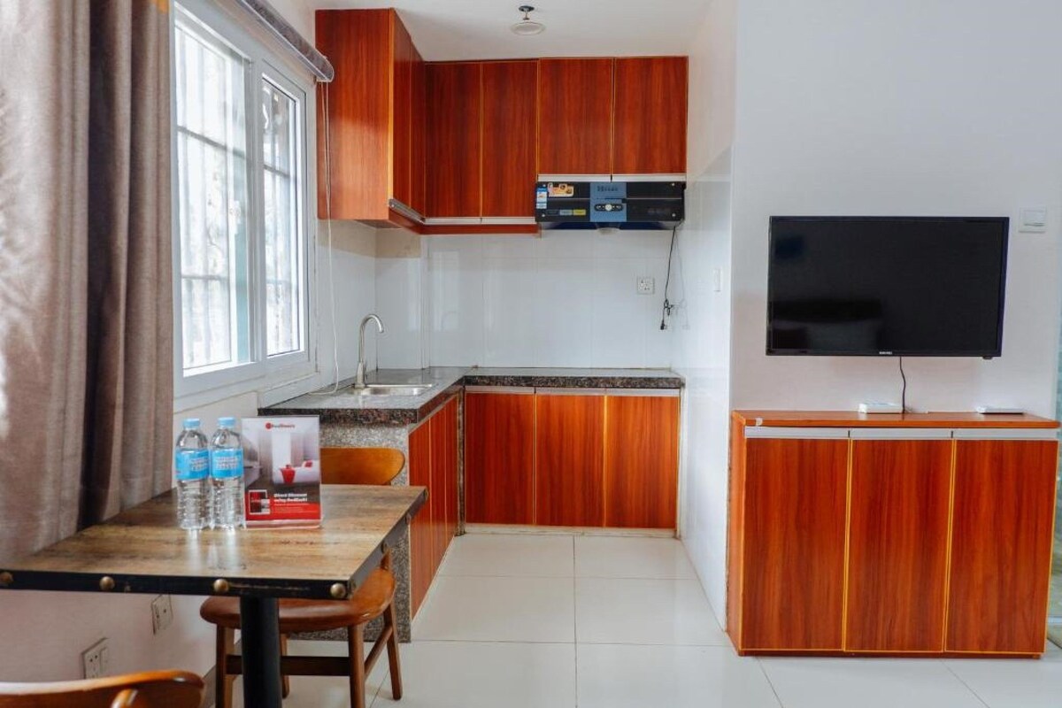 A compact kitchen with wooden cabinets, a built-in microwave, and a flat-screen TV.