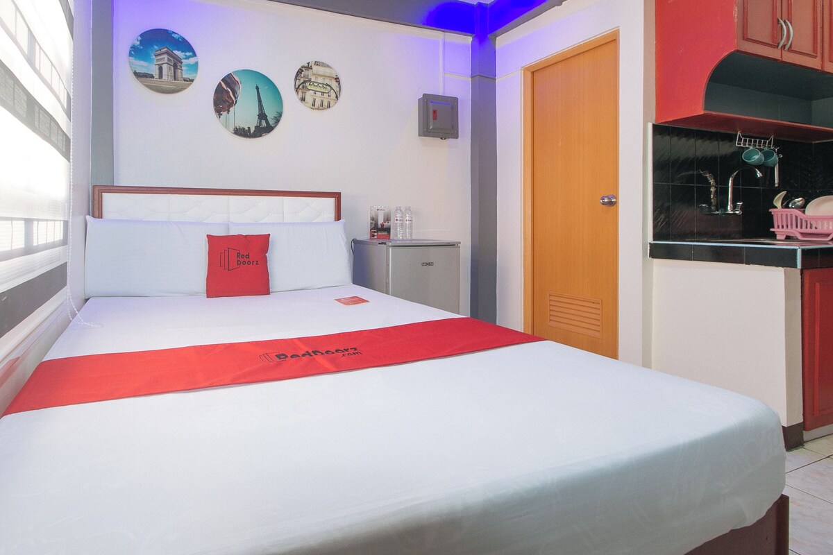 A hotel room with a bed, a red throw, a minibar, a door, and wall decorations.