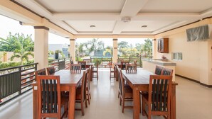 A spacious outdoor dining area with wooden tables and chairs, a balcony with a railing, and a view of greenery and buildings in the background. - RedDoorz Plus @ Santa Catalina Metro Vigan (Santa Catalina)