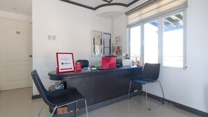 A reception area with a desk, two black chairs, a red laptop, and a window with blinds. - RedDoorz Plus @ Santa Catalina Metro Vigan (Santa Catalina)