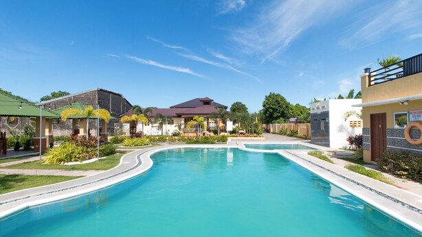 A swimming pool with a curved design, surrounded by buildings with a mix of architectural styles, including a house with a dark roof and a building with a light-colored facade. - RedDoorz Plus @ Santa Catalina Metro Vigan (Santa Catalina)