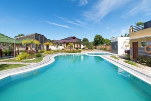 A swimming pool with a curved design, surrounded by buildings with a mix of architectural styles, including a house with a dark roof and a building with a light-colored facade. - RedDoorz Plus @ Santa Catalina Metro Vigan (Santa Catalina)