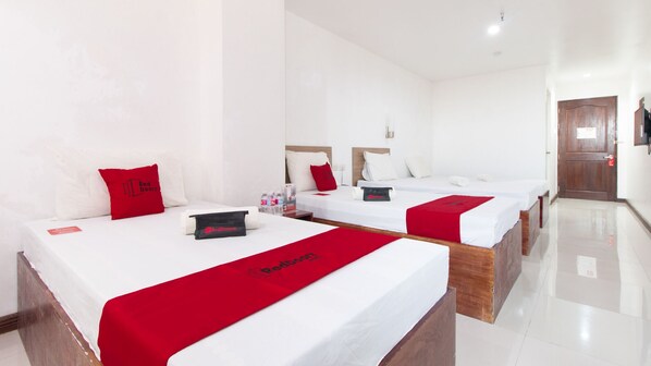A hotel room with two beds, each with a red bedspread and pillows, a small table with toiletries, and a wooden door.