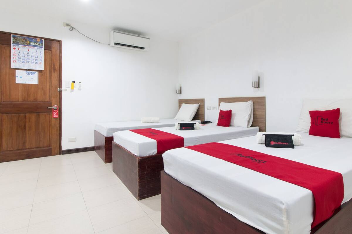 Habitación de hotel con dos camas individuales, una puerta de madera, un calendario, un equipo de aire acondicionado y una toalla de RedDoorz.