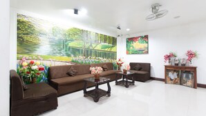 A living room with a large mural, a sofa, two armchairs, a coffee table, and a side table with flowers. - RedDoorz Plus near Vigan City Commercial Center (Vigan)