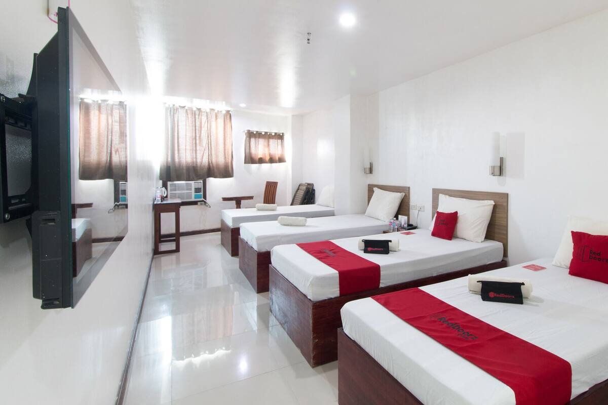 Habitación de hotel con cuatro camas, un escritorio, una silla, un televisor y una ventana con cortinas.