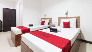 A hotel room with two beds, each with a red bedspread and pillows, a wooden headboard, and a small bedside table with a bottle and a tissue box. - RedDoorz Plus near Vigan City Commercial Center (Vigan)